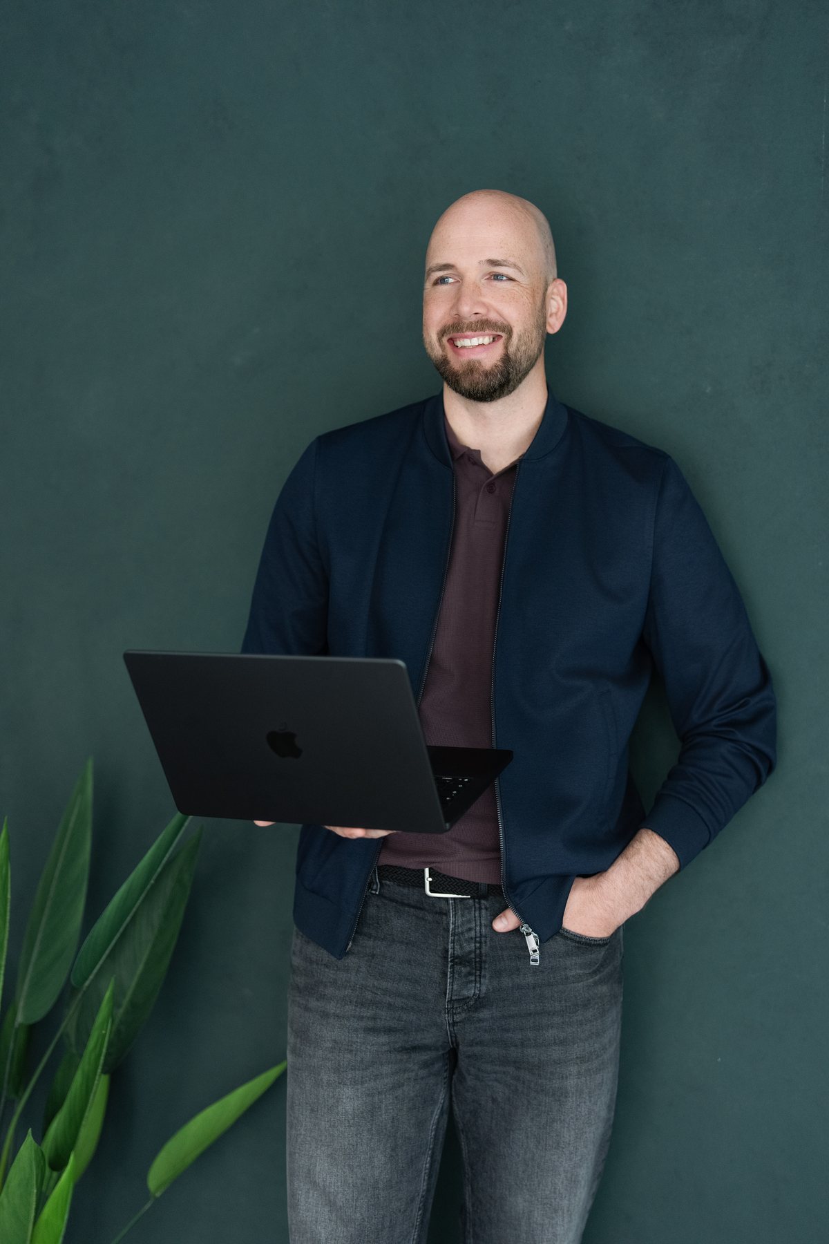 René Wienhold stehend mit Laptop vor grüner Studiowand